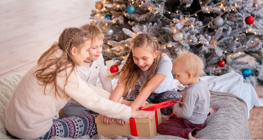 Siblings opening a present in the living room next to a Christmas tree.